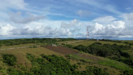 Vista-Aérea-De-Idílicas-Tierras-De-Cultivo-Y-Exuberantes-Campos-Con-Torre-De-Satélite-Y-Un-Impresionante-Paisaje-Nublado-En-Segundo-Plano.