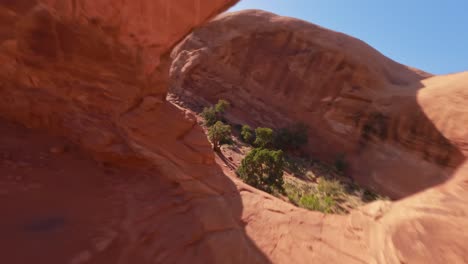 an fpv drone flying under the red sandstone funnel arch in the sandy and rocky desert of moab utah