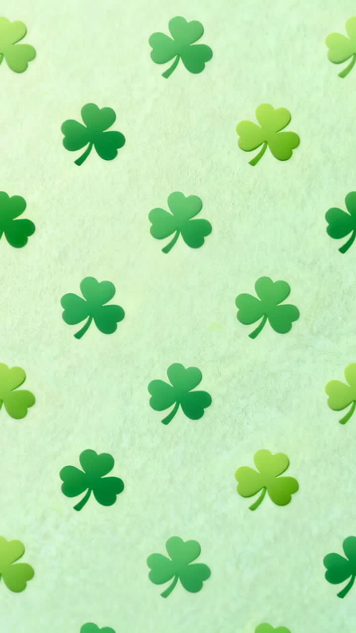 Vertical video: Shifting repeating green three-leaf clover pattern on pale paper, leaf passing lens