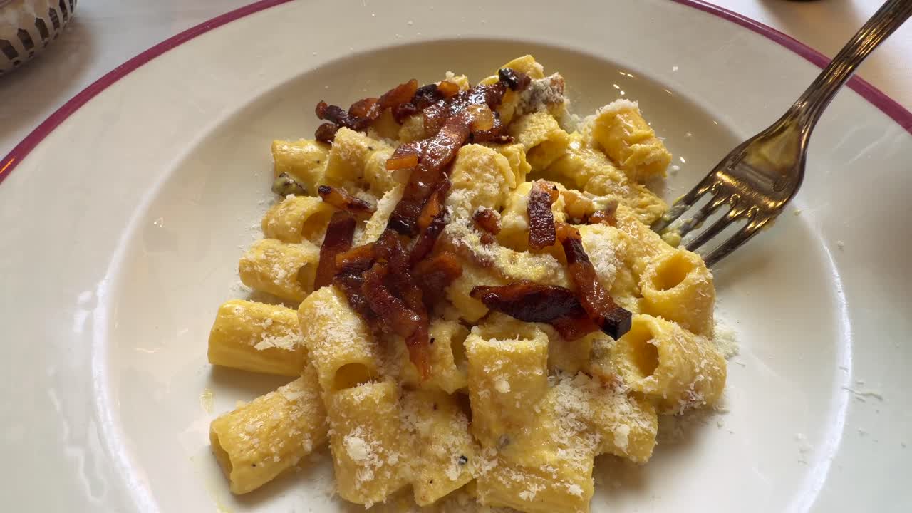 Forchetta che raccoglie deliziosi rigatoni alla carbonara con pancetta e formaggio.