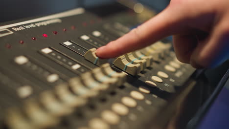 close-up of hand adjusting sliders on lighting control board. adjusting brightness on digital lighting controller. equipment for stage, theater, or event lighting control in use with real-time settings