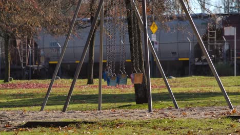 Empty swings in park with passing train in background, sunny day