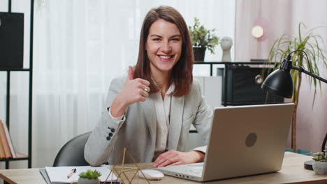 Mujer-De-Negocios-Que-Trabaja-En-Una-Computadora-Portátil-Mirando-Con-Aprobación-A-La-Cámara-Muestra-Los-Pulgares-Hacia-Arriba-Y-Muestra-Retroalimentación-Positiva