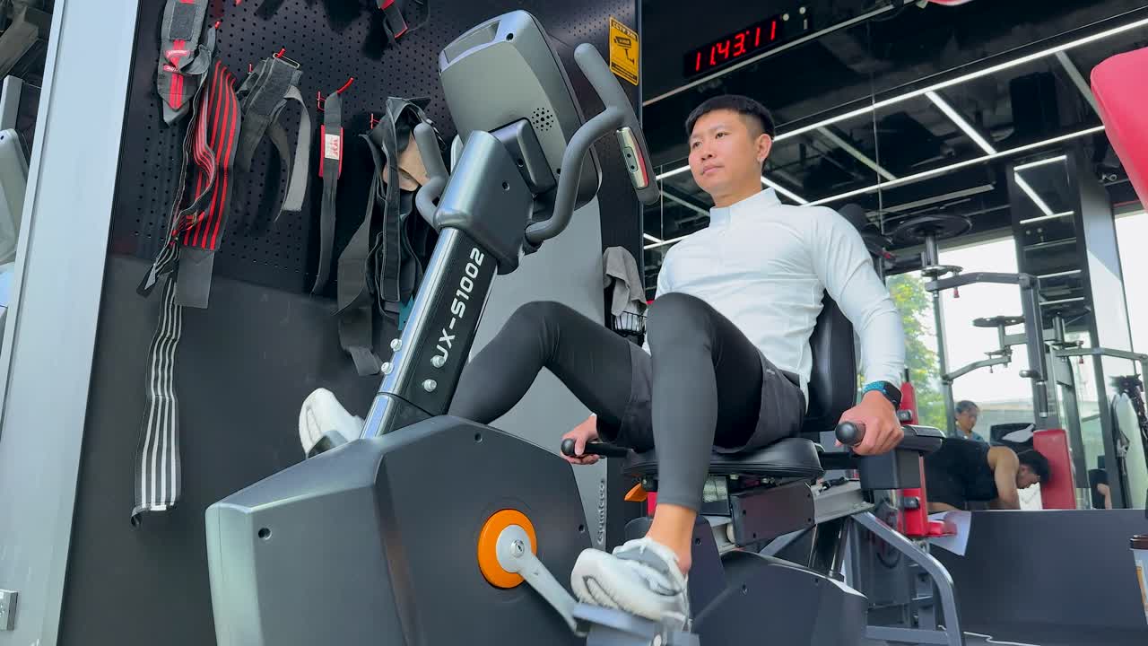 Athletic man training on a recumbent bike in a bright, modern gym with large windows