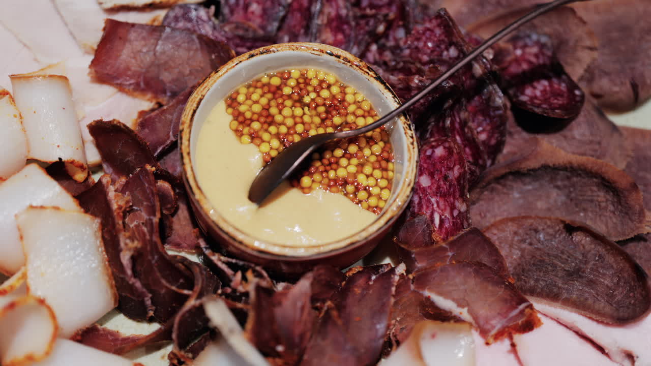 Gourmet charcuterie board with assorted cured meats, smoked slices, and a mustard seed sauce served in a bowl