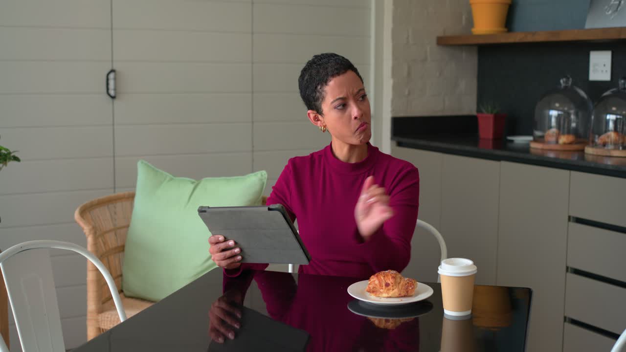 Donna afroamericana sui 30 che usa un tablet, legge e assaggia il caffè per valutarne l’aroma in cucina