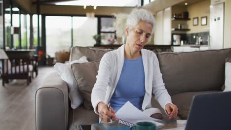 senior mixed race woman sitting on sofa taking notes