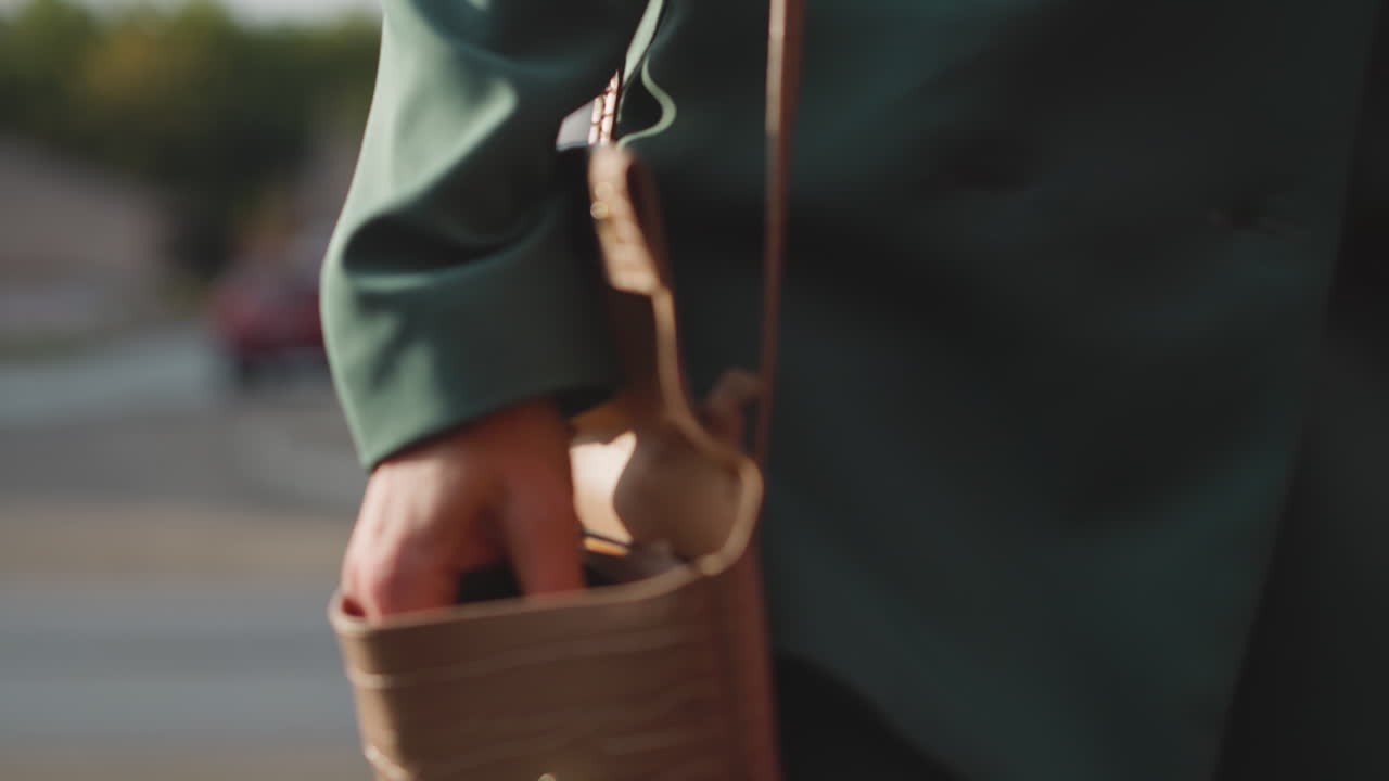 초록색 슈트 입은 여자가 거리에서  ⁇ 는 가방에서 전화를 꺼내