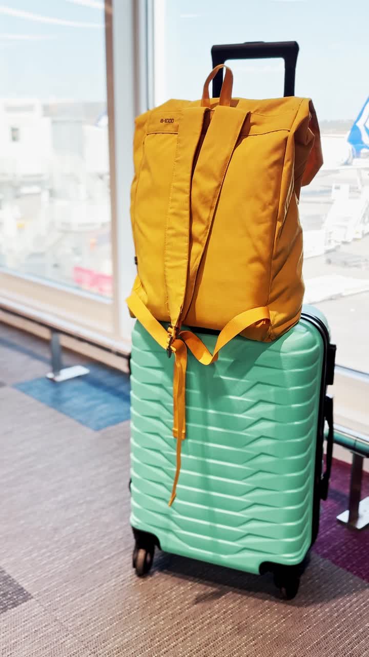Teal Suitcase and Yellow Backpack by Airport Window with Plane