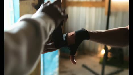 African American male trainer assisting boxer in wearing hand wrap in gym 4k