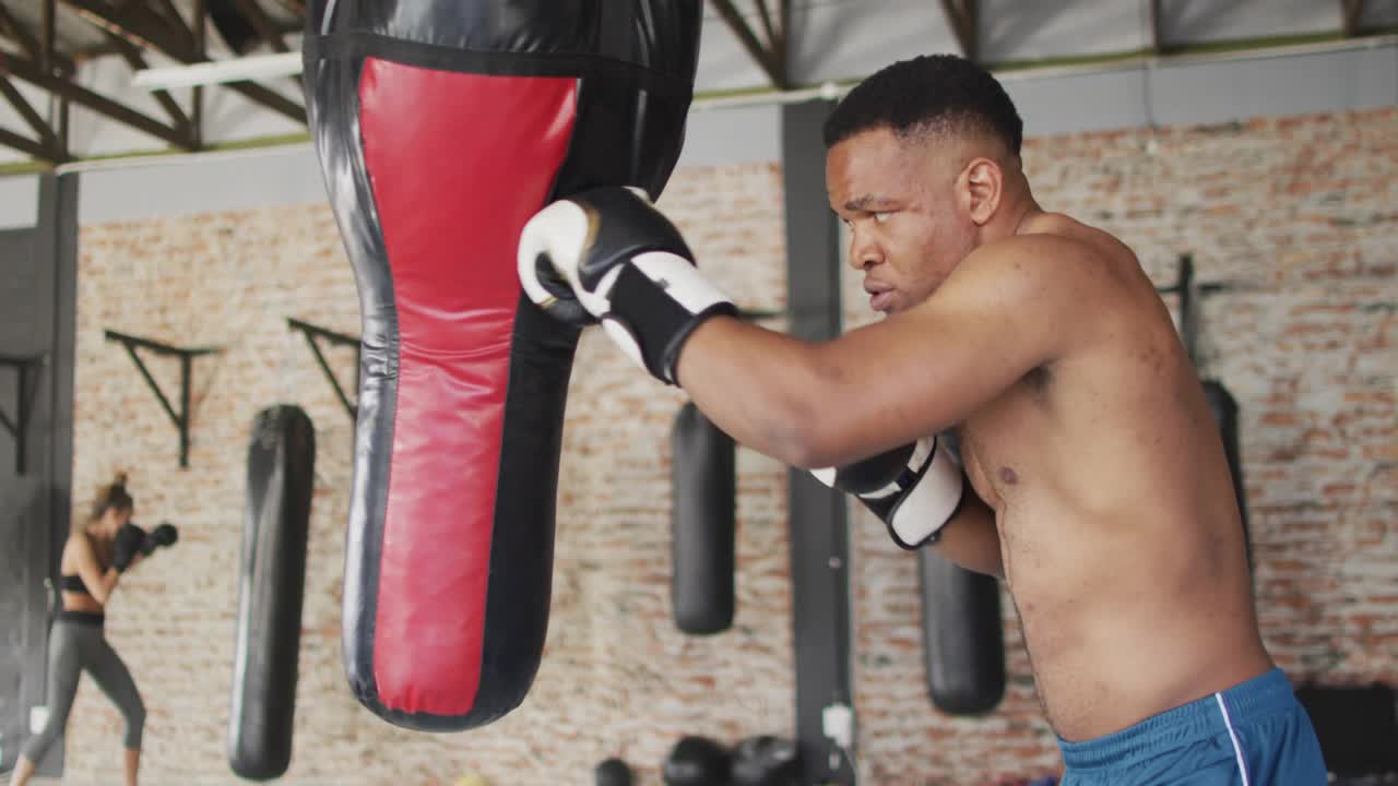 Male boxer entering frame, throwing jabs, hooks at heavy bag, blue sparks, camera closing, training