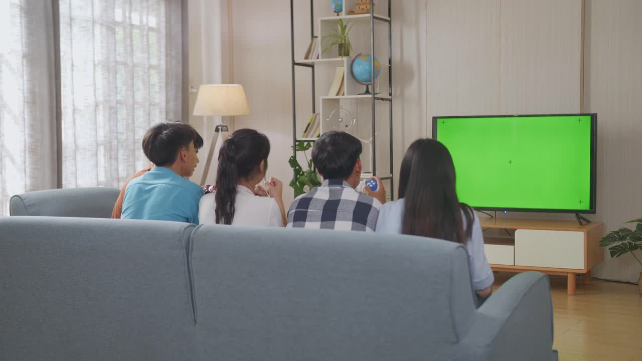 아시아 십대들이 tv 녹색 스크린으로 비디오 게임을 하고 집에서 승리를 축하합니다.