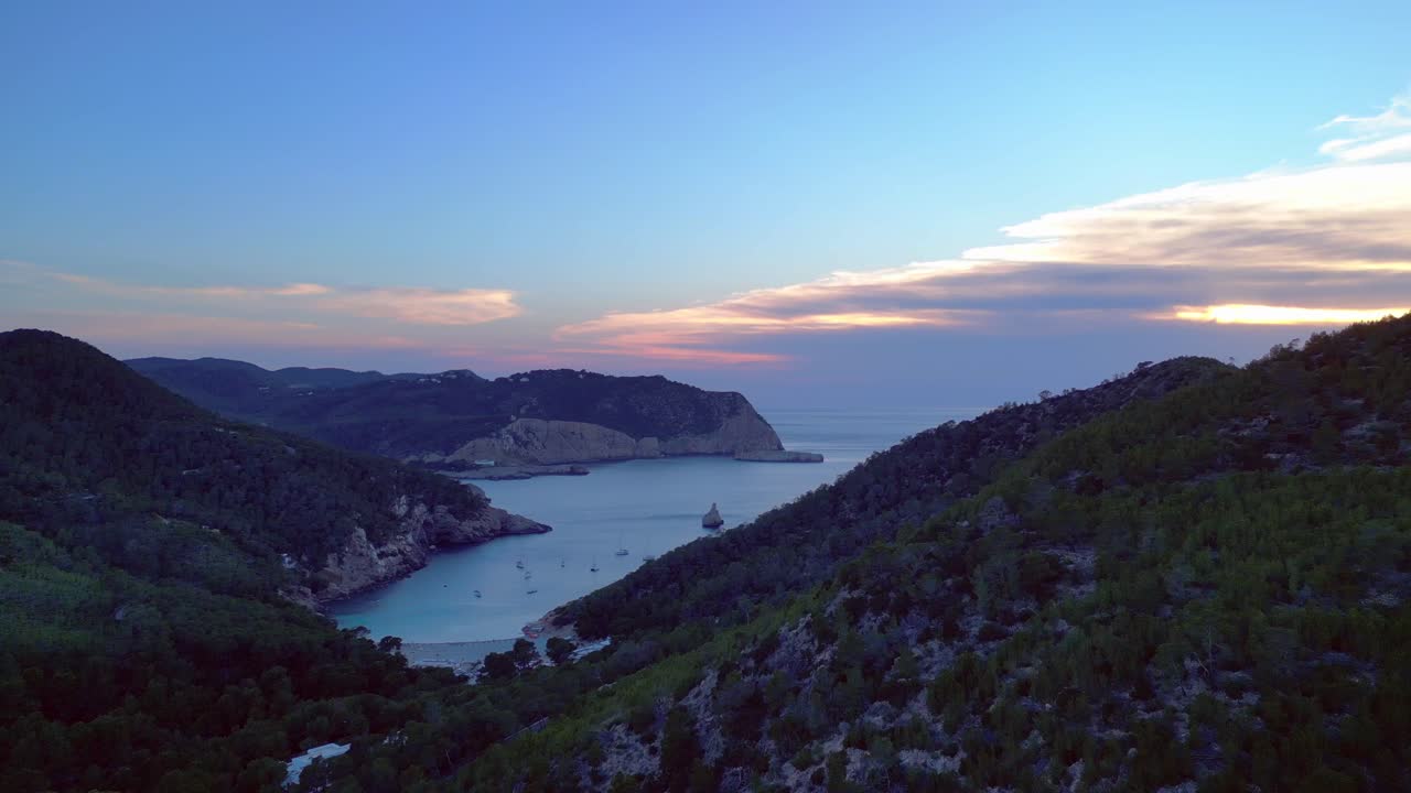 panoramic view of Cala Benirras bay and wooded hills at dusk in Ibiza. Great aerial view flight fly push forward drone