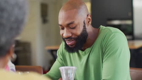 Video-of-happy-african-american-father-smiling-and-eating-at-family-breakfast-table