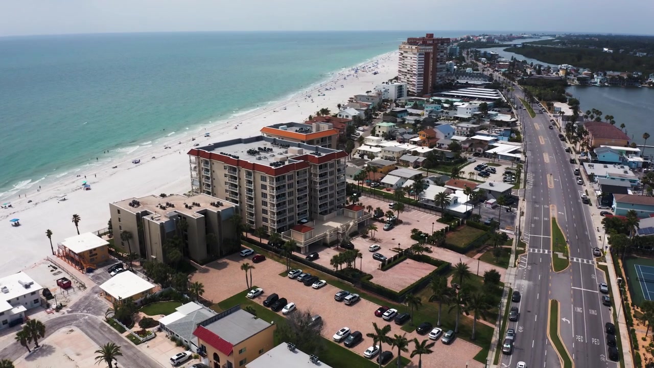 Imágenes aéreas capturan la combinación de edificios residenciales, carreteras y la extensa playa de arena blanca en Indian Shores. Adecuado para exhibiciones inmobiliarias o reportajes de viajes.