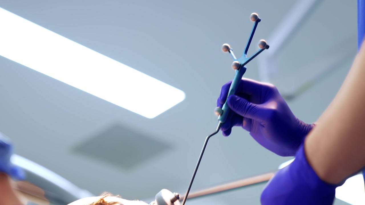 Hands in blue latex gloves holding a neurosurgical probe at the head of the patient. Brain surgery concept.
