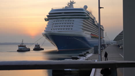 large cruise ship and tugboats at port during golden hour
