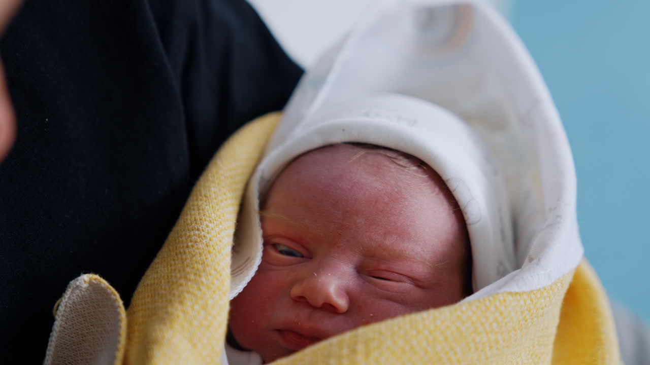 Red face of a newborn baby covered in blankets. Lovely child falling asleep in parent's arms. Close up.