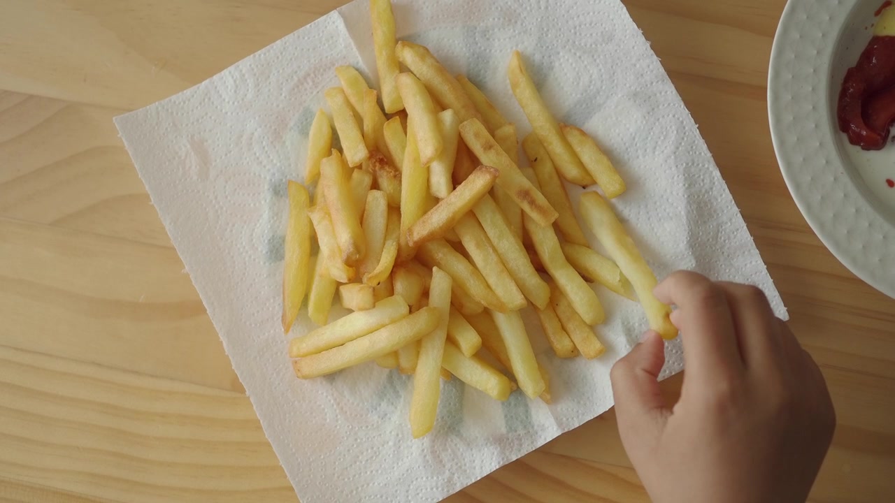 Mano di un bambino che prende una patatina fritta da un tovagliolo di carta