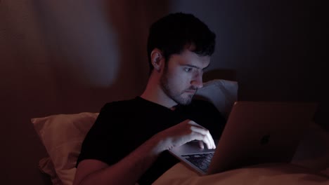 hombre con computadora portátil en la cama, internet en línea por la noche, trabajo tardío, navegación web, video viendo en el cuaderno antes de dormir