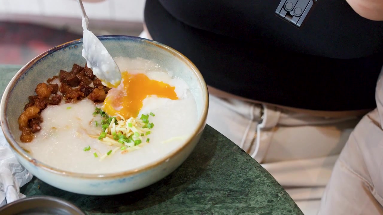 Rekaman jarak dekat seseorang menggunakan sendok untuk mencampur kuning telur ke dalam bubur gurih