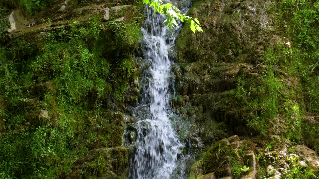 cascada de maries, rodeada de exuberante vegetación verde y rocas cubiertas de musgo, rayos de sol, isla de thassos, grecia