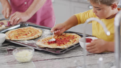 Happy-caucasian-grandfather-and-grandson-making-pizza-in-kitchen,-slow-motion