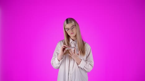 joven dama rubia blanca limpiar sus uñas con gafas y sexy inteligente mirada en croma estudio fondo rosa, torso modelo mujer vista