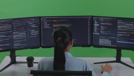 그린 스크린 스튜디오에서 여러 화면으로 코드를 작성하기 위해 컴퓨터를 사용하는 아시아 여성 개발자의 뒷면