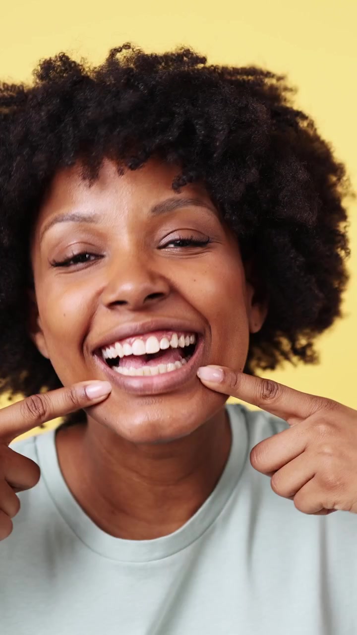 Mulher Negra Feliz com Cabelo Afro Apontando para Seus Dentes Brancos e Saudáveis