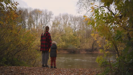 Tranquilo-Viaje-De-Fin-De-Semana-En-La-Naturaleza-Un-Niño-Pequeño-Con-Su-Madre-Está-Parado-En-El-Bosque-Y-Mirando-El-Lago-Disfrutando-Del-Paisaje-En-El-Entretenimiento-Familiar-Del-Día-De-Otoño-Juntos