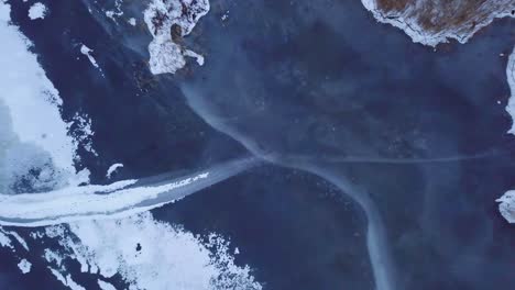 vista aérea de pájaro del lago congelado liepaja durante el invierno, hielo azul con grietas, islas secas de juncos amarillentos, día de invierno nublado, disparo ascendente de drones