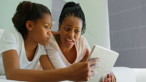 Front-view-of-mid-adult-black-mother-and-daughter-using-digital-tablet-on-bed-in-comfortable-home-4k