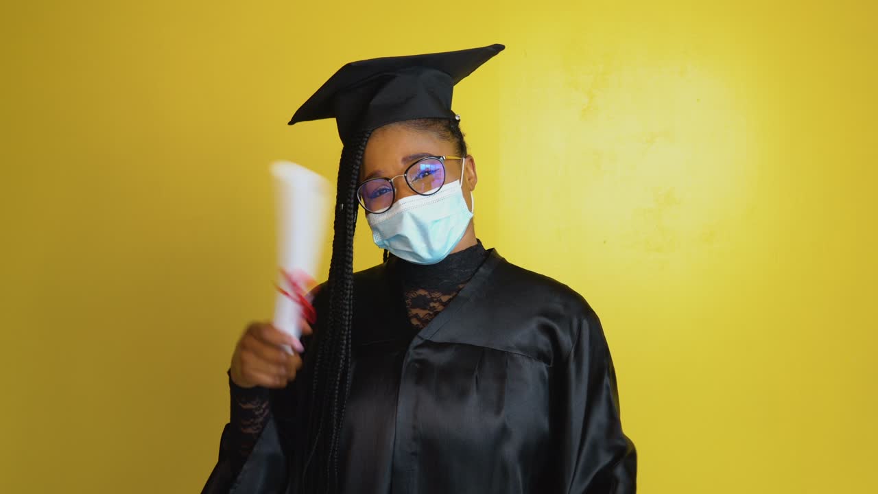 The african american female graduate student in a protective mask and with a diploma in hand expresses the gesture of the need to comply with quarantine security measures. Education concept