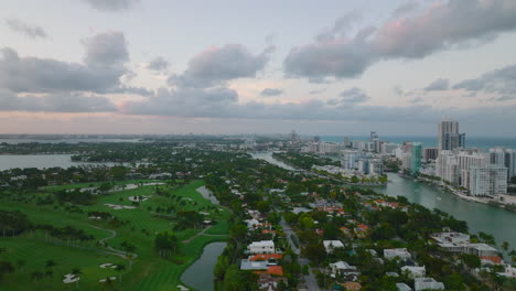 Aerial-view-of-residential-borough-at-dusk.-Sliding-reveal-of-golf-course-with-palm-trees.-Miami,-USA