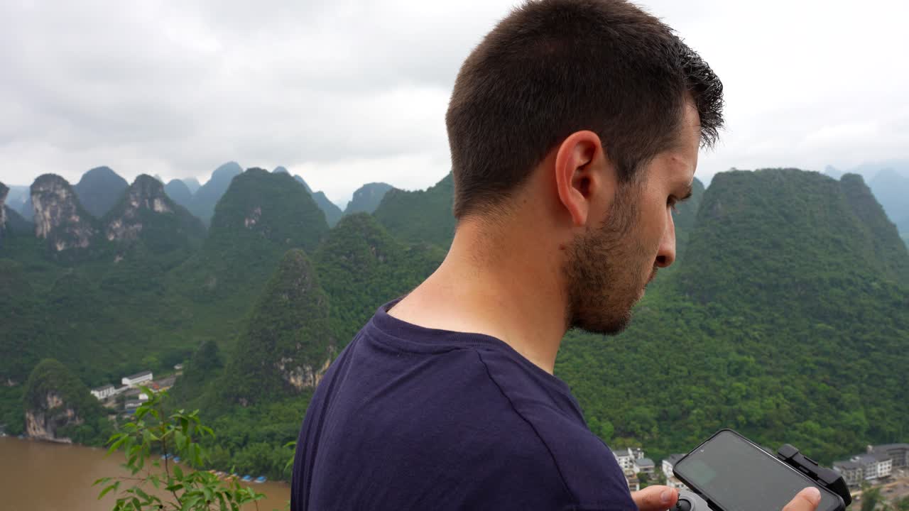 중국 핑의 카르스트 산맥 주변을 날아다니는 원격 제어 장치에 연결된 스마트폰을 사용하는 드론 조종사