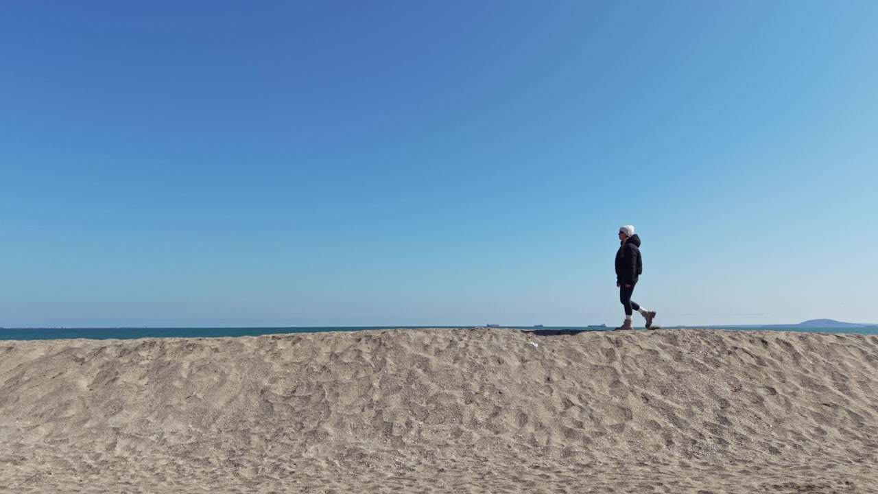 Spacer po piaszczystej plaży pod czystym, błękitnym niebem ze spokojnym oceanem w tle w ciągu dnia