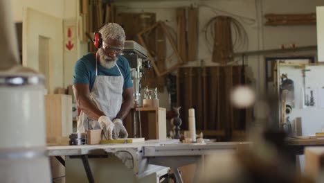 afrikaans-amerikaanse mannelijke timmerman die tafelzaag gebruikt om hout te snijden in een timmerwerkplaats