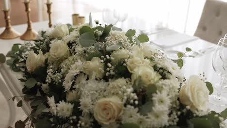 lush white flower arrangement with roses and baby's breath on an elegant wedding table