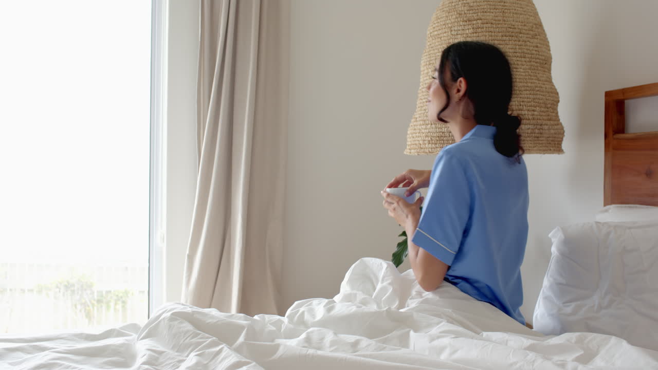 woman in pajamas enjoying morning coffee in cozy bedroom, at home
