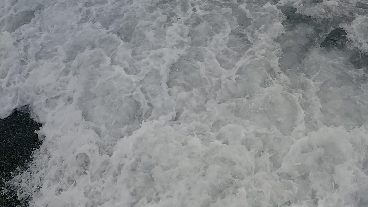Top-Down Perspective of Foamy Waves Splashing onto a Philippine Coastal Beach at Looc Bay