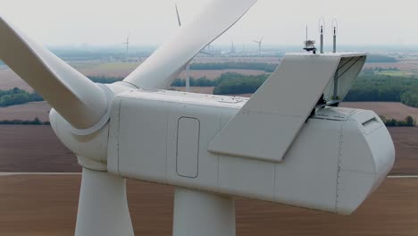 wind turbine farm close up of nacelle from rear using a drone panning around with farmland in the background