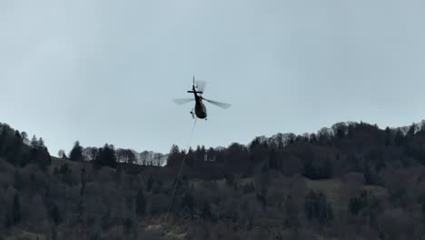 un helicóptero flota sobre los bosques de suiza, demostrando operaciones aéreas en entornos boscosos y varias tareas que involucran cuerdas
