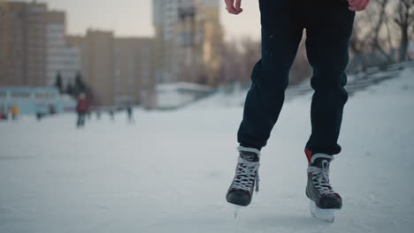 close up of people skating on frozen lake near urban buildings, ice surface with skate marks and snow, focus on legs wearing skates, blurred background featuring skaters and cityscape