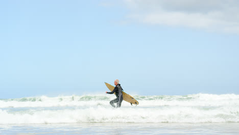 seitenansicht von einem alten kaukasischen älteren mann, der mit einem surfbrett am strand 4k läuft