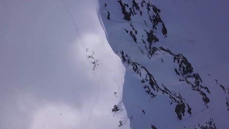 Aerial-view-from-drone-looking-down-on-mountain-ridge-covered-with-snow-and-footprints-following-ridge-toward-peak