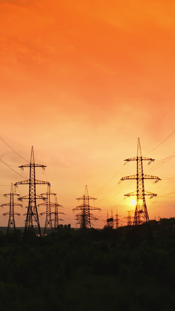 Electricity pylons at sunset. Transmission towers. Silhouette of high-voltage electic towers that transport electric power from generating stations to electrical substations. Aerial view. Vertical video