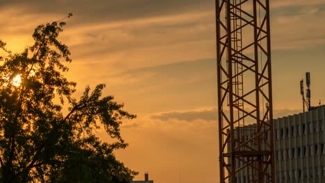 timelapse of the undergoing sun in orange shades of colors with the part of a crane and a building as foreground elements