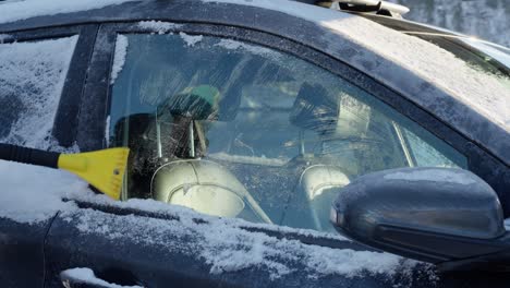 a person scrapes snow and ice off a car side window in cold winter conditions. closeup with window filling frame