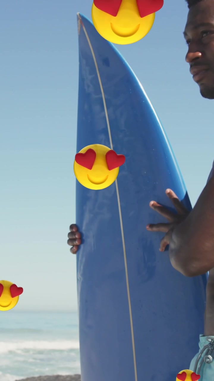 Multiple heart eyes emojis floating against african american man with surfboard on the beach